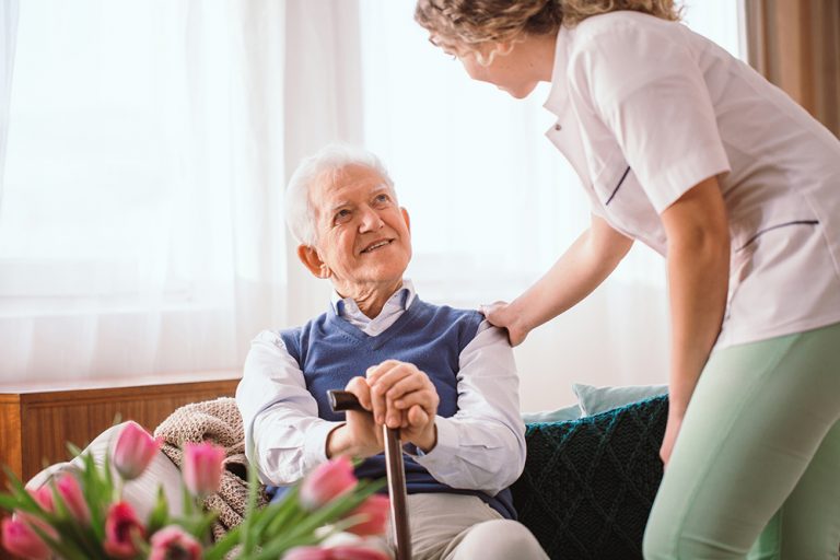 Senior man with a walking stick being comforted by nurse in the hospice
